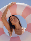 Woman holding a pink and white striped pool float against a blue sky.